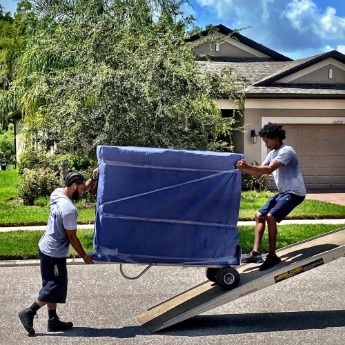 Two Employees of Dunedin Moving Company Loading a Heavy Furniture With a Trolley
