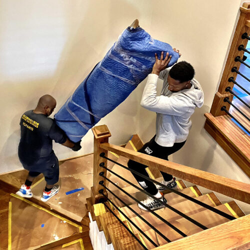 Employees of a Trinity FL Moving Company Lifting a Furniture Up the Stairs