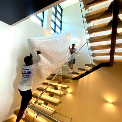 Two Moving Company Employees Carrying a Heavy Furniture Down The Stairs of Stonelake Ranch House