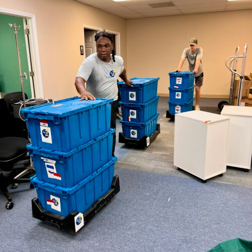 Office and Industrial Moving Company Servicing Tampa Florida Employees of Tampa-based Office and Industrial Moving Company Pushing Blue Crates